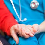 Nurse and senior care at home patient holding hands